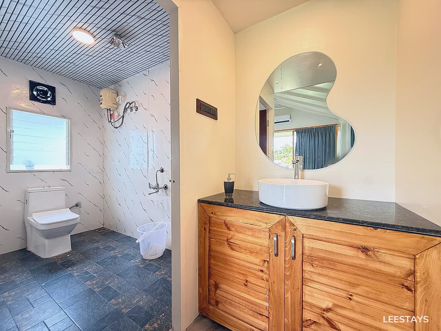 A bathroom with a white toilet on the left and a wooden vanity with a white sink and a unique mirror on the right.