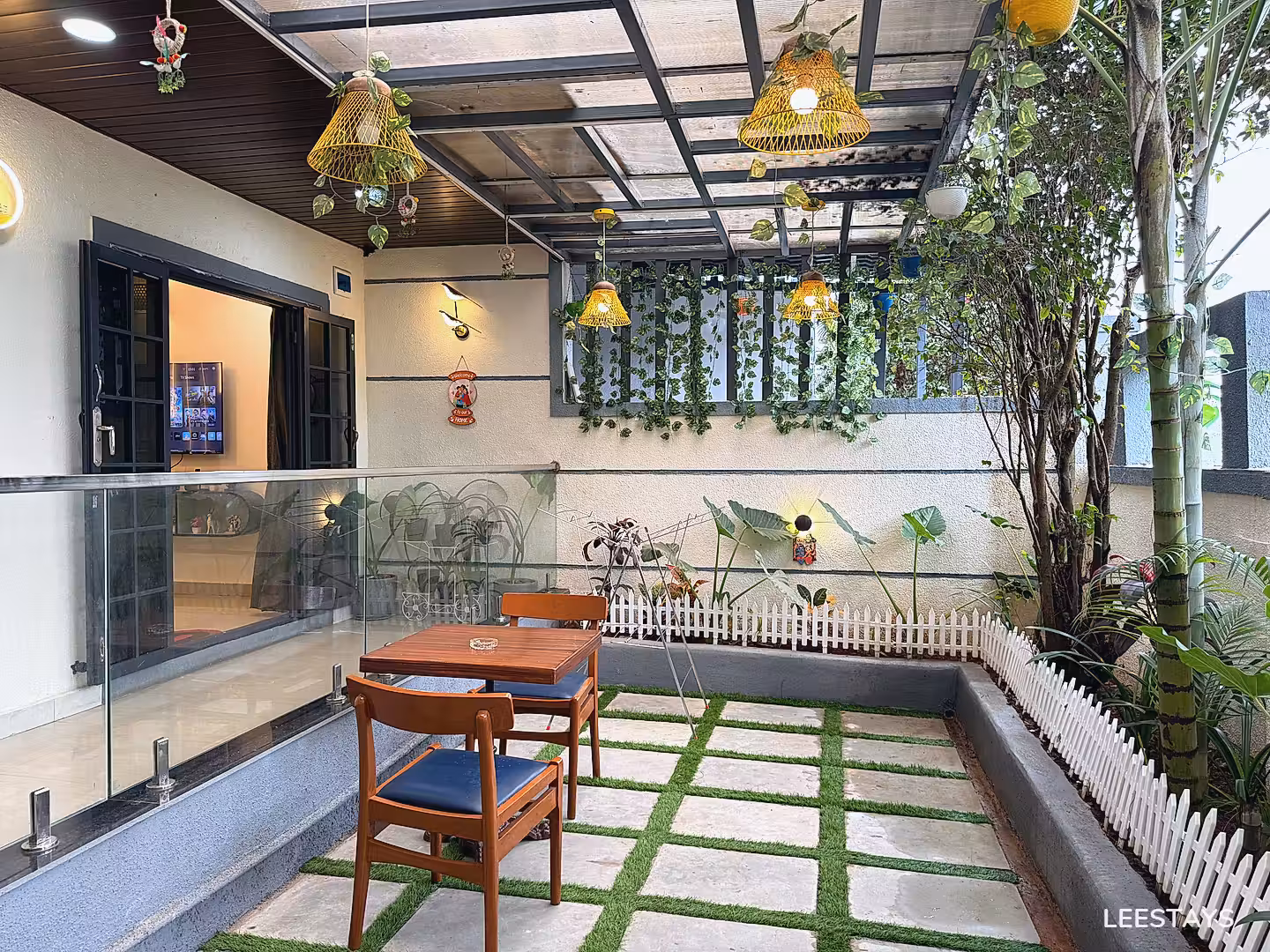 Outdoor seating area with two wooden chairs and a table, under a covered patio with hanging lights and greenery.