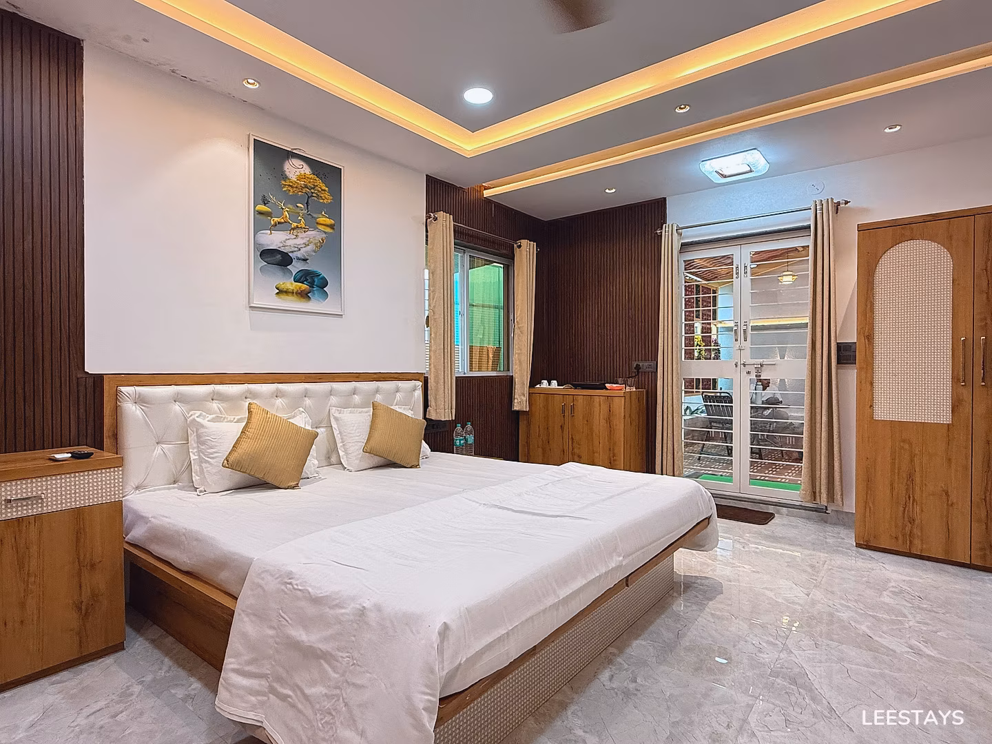 Bed with white linens, pillows, and a tufted headboard in a room with wooden accents and a painting on the wall.