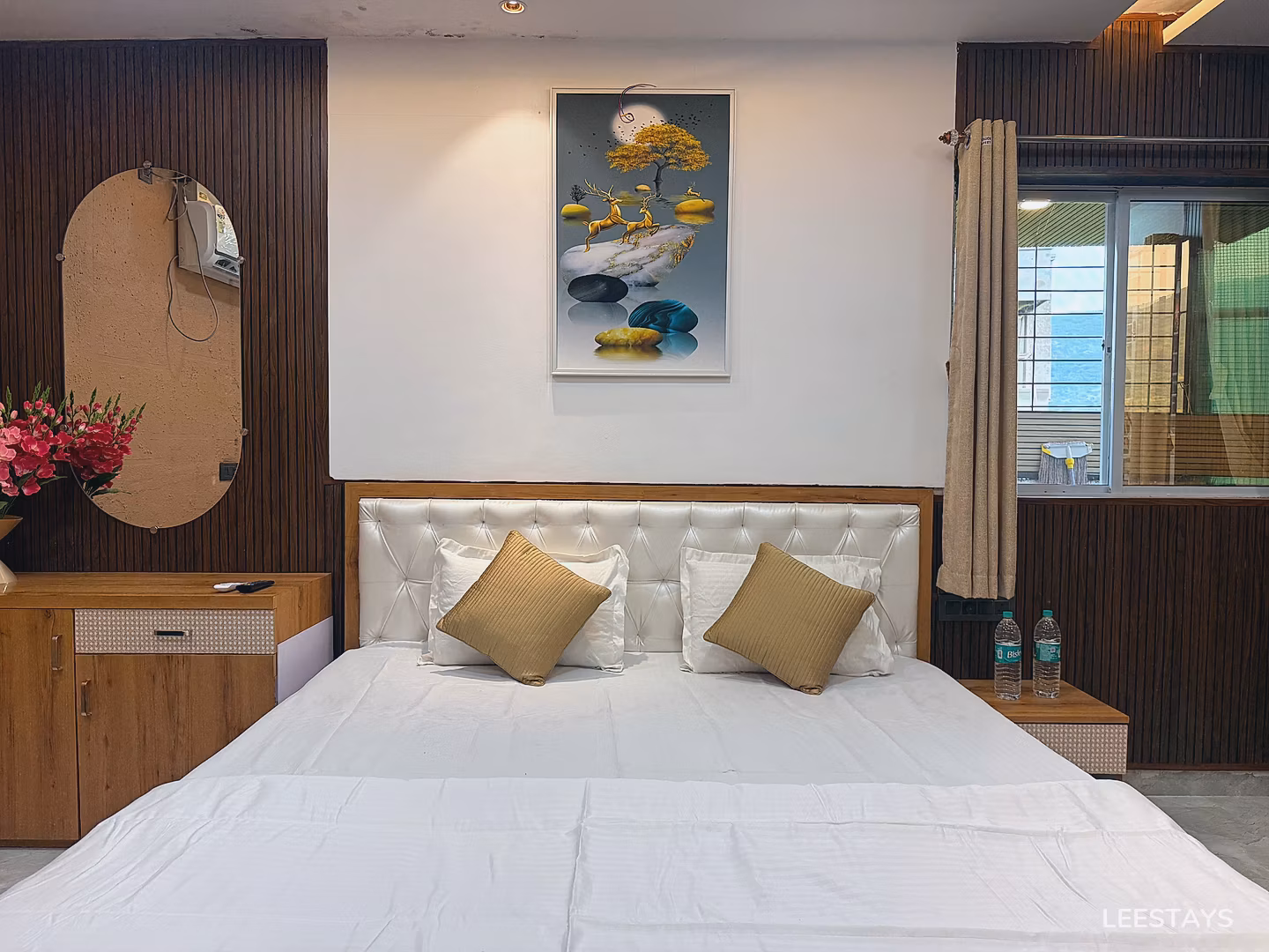 Bed with white linens, upholstered headboard, and two gold square accent pillows. A painting of deer and a tree hangs on the wall above the headboard.