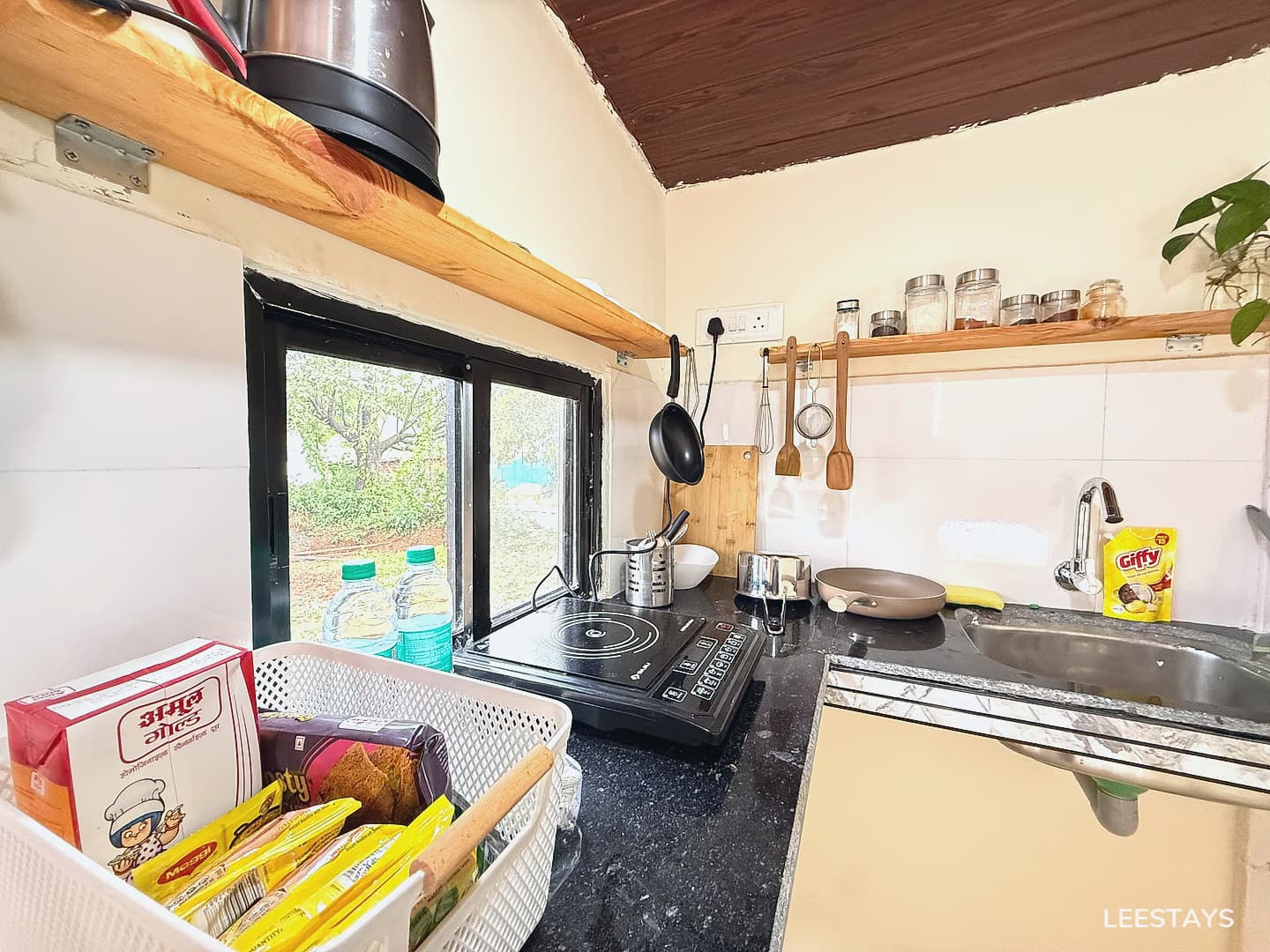 Kitchenette counter with a sink, induction stove, cooking utensils, and a basket of food items.