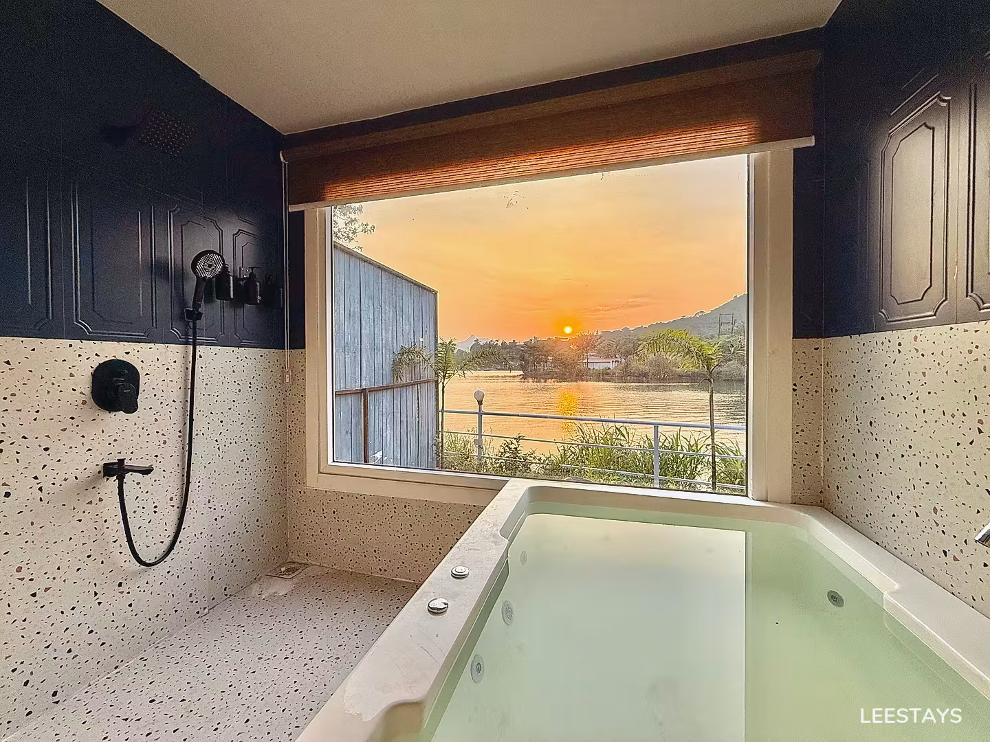 Corner of a bathroom with a large tub and a walk-in shower, overlooking a sunset over a body of water.