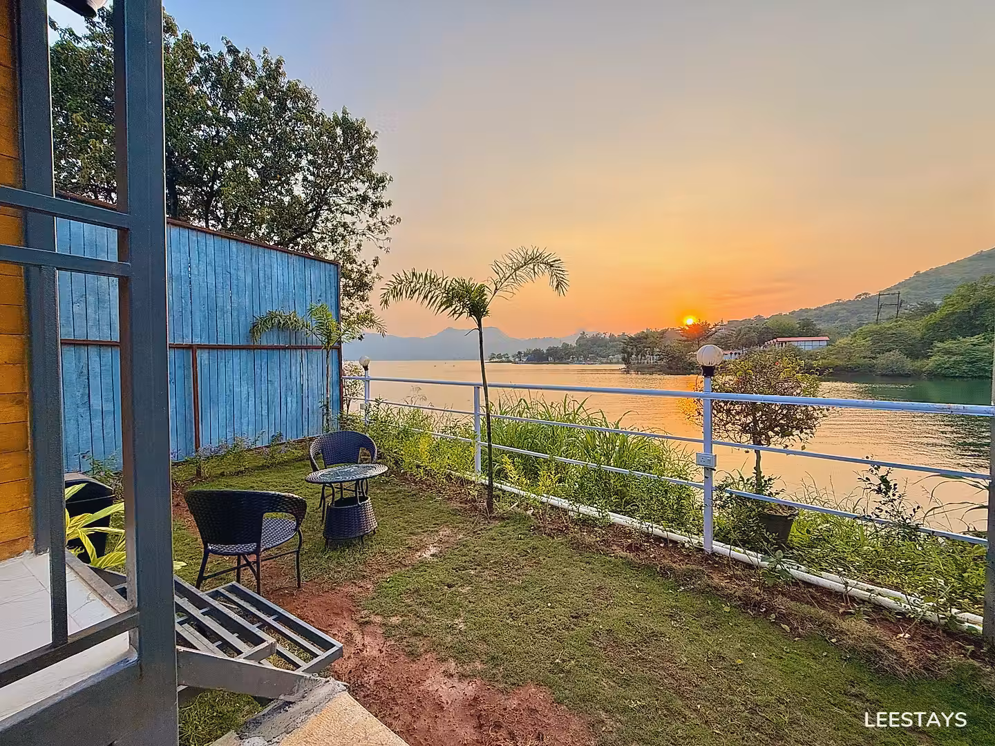 Outdoor seating area with chairs and a table by a lake at sunset.