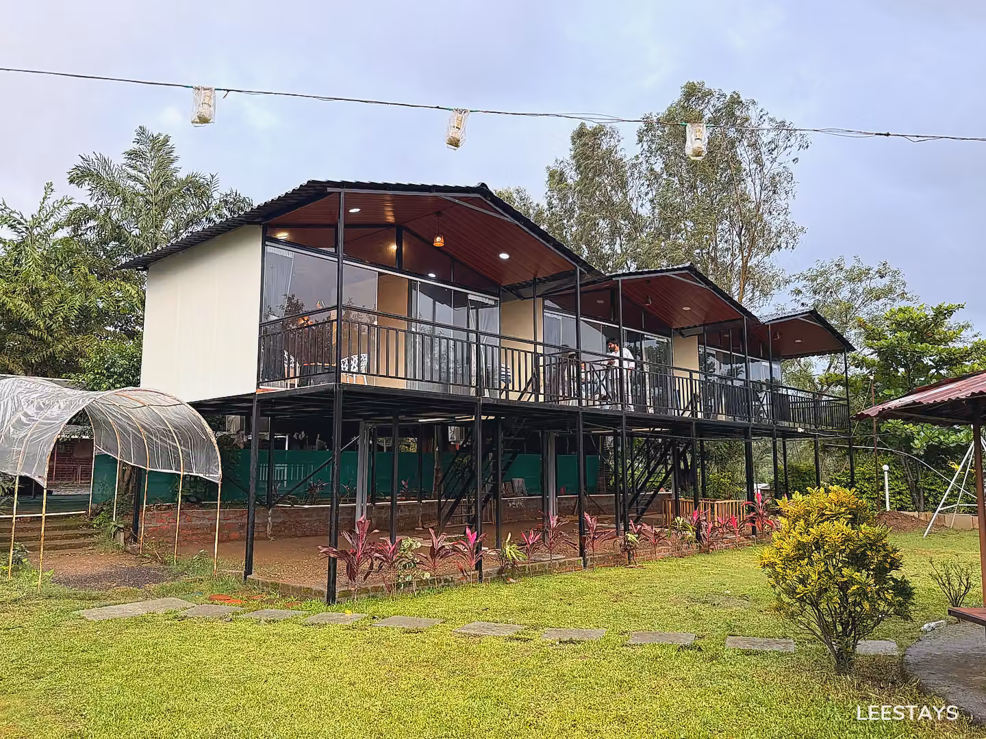 Two-story elevated rooms with balconies and glass walls overlook a grassy area with trees and plants.