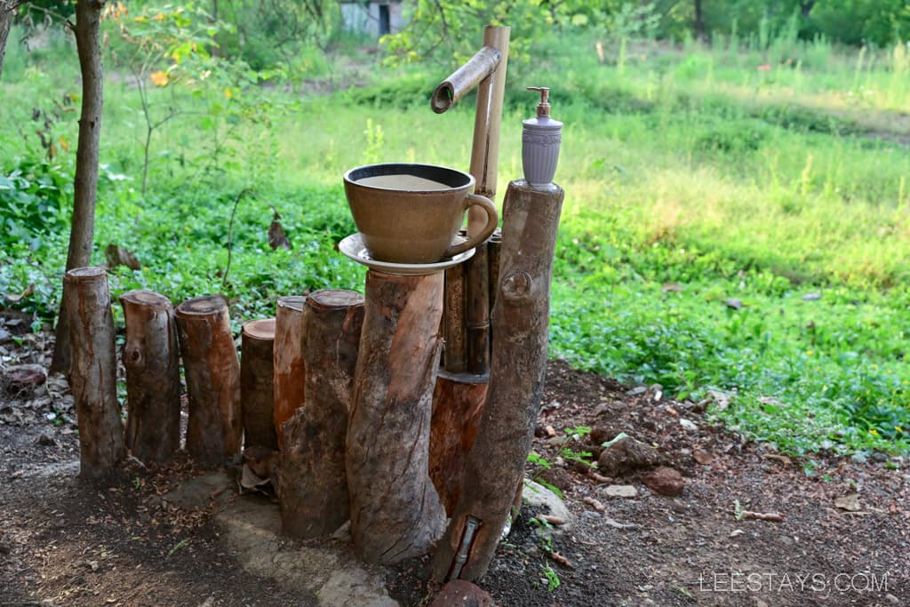 A handwashing station made of wooden logs featuring a bowl and a soap dispenser on a platform.