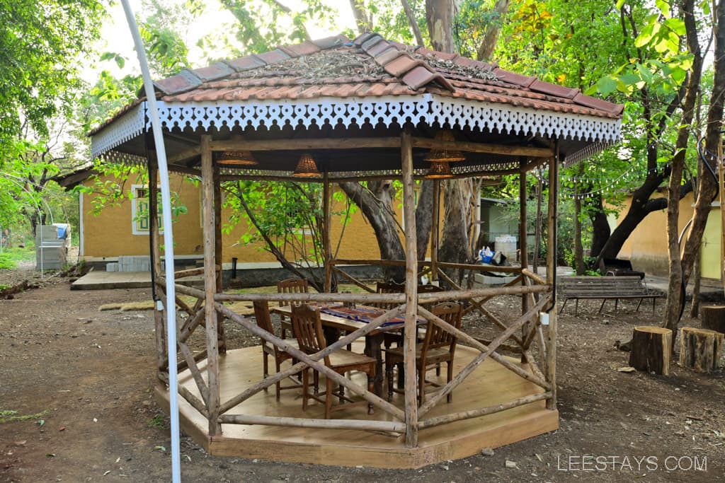 Wooden gazebo structure with a tiled roof and wooden seating arranged around a table.