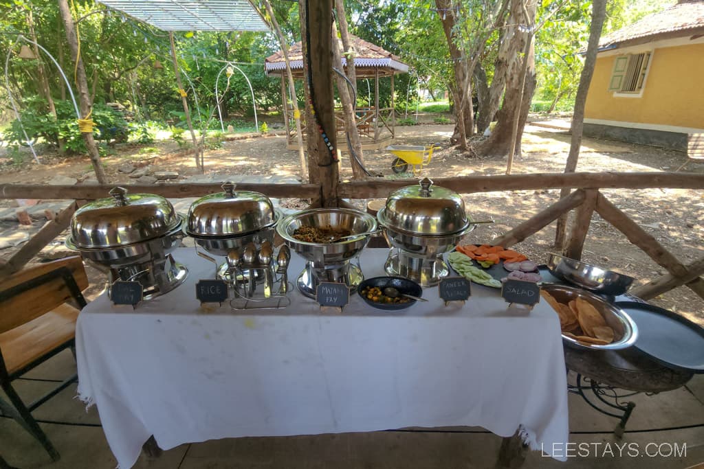 Buffet table displaying three silver food containers labeled rice, fish fry, and curry, alongside a salad and assorted items.