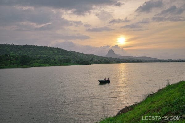 Sunset view over Malvandi Lake with a small boat on the water, situated near the Dome Story Resort, surrounded by lush green hills.