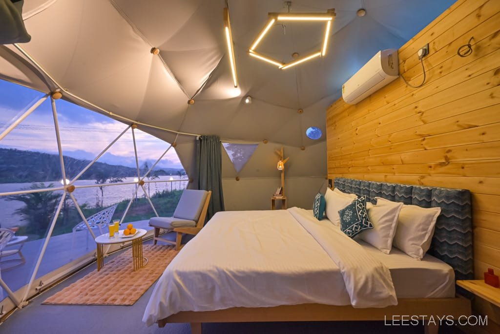 Interior of a dome-shaped room at Dome Story Resort near Malvandi Lake, featuring a large bed with decorative pillows, wooden walls, and a view of the lake through a geometric window.