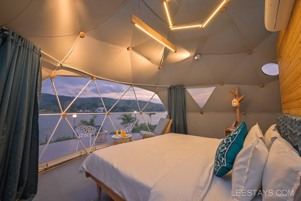 Interior of a dome structure at Dome Story Resort, Malvandi Lake, featuring a cozy bed, modern lighting, and views of the lake through large, geometric windows.