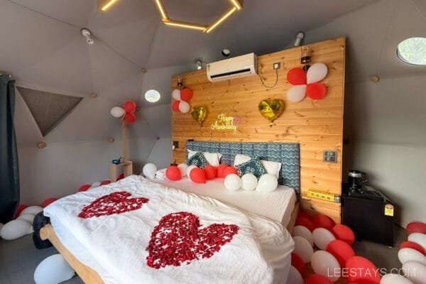 A decorated bedroom inside Dome Story Resort near Malvandi Lake, featuring a neatly made bed with a heart-shaped petal arrangement and red and white balloons for an anniversary celebration.