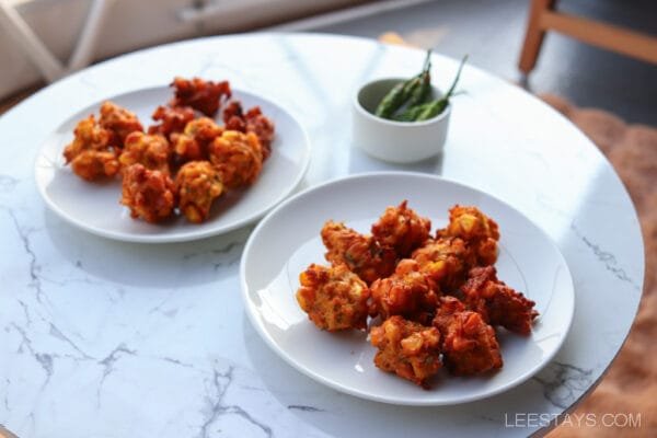 Two plates of fried snacks on a marble table with a bowl of green chilies at Dome Story Resort, Malvandi Lake.