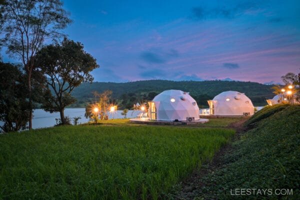 Geodesic domes illuminated at dusk at Dome Story Resort near Malvandi Lake, surrounded by green landscape and trees.