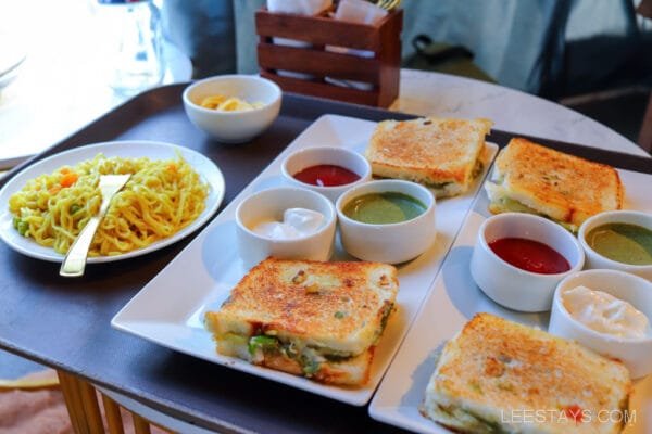 A meal served at Dome Story Resort, Malvandi Lake, featuring grilled sandwiches with various dipping sauces and a plate of noodles with vegetables.