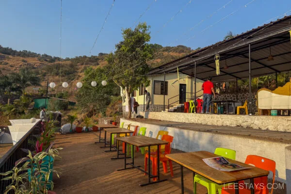 Glamping site near Pawna Lake featuring a patio with colorful chairs, wooden tables, and a view of surrounding hills under a clear blue sky.