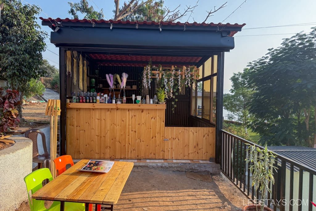 Rustic wooden bar area with colorful chairs at a glamping site near Pawna Lake, surrounded by greenery and a relaxing outdoor atmosphere.