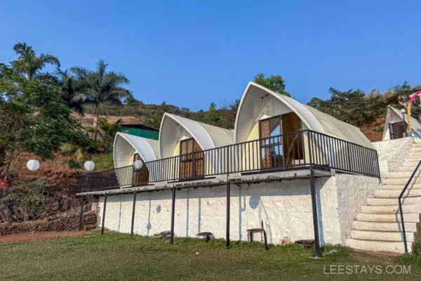 Elegant glamping units near Pawna Lake, featuring modern architecture with large windows, set against a backdrop of lush greenery and clear blue skies.