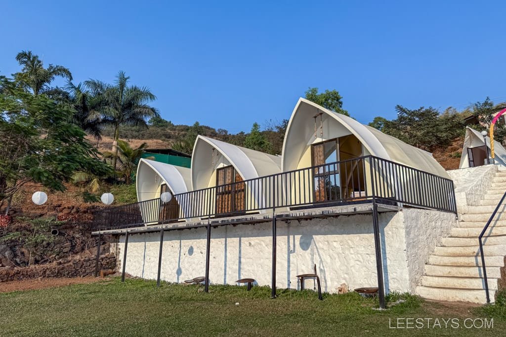 Elegant glamping units near Pawna Lake, featuring modern architecture with large windows, set against a backdrop of lush greenery and clear blue skies.