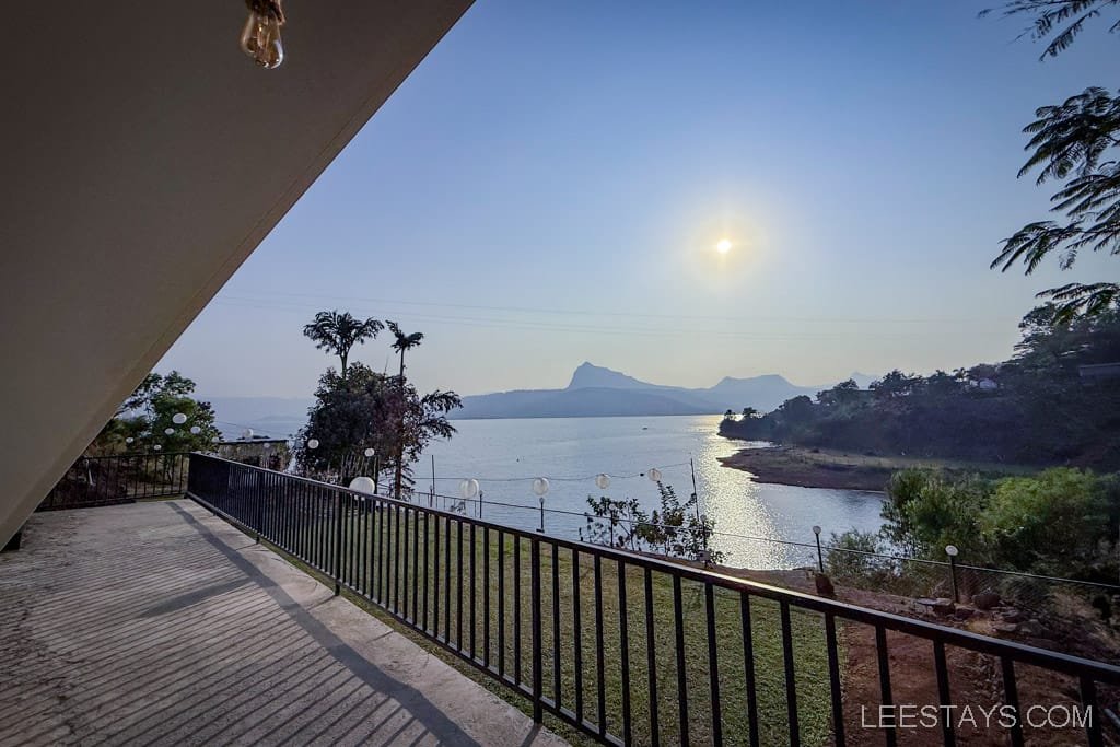 Scenic view of Pawna Lake from a luxurious glamping site, with a clear sky and lush greenery in the background, ideal for relaxation.