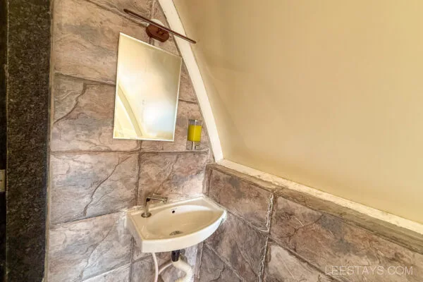 Elegant washbasin setup with modern amenities for a glamping experience near Pawna Lake, featuring stylish stone-textured walls and a sleek mirror.