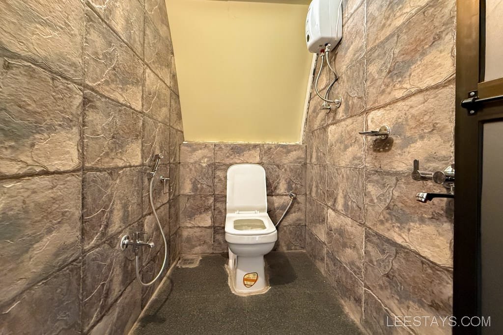 Modern stone-walled bathroom with sleek fixtures, suitable for a glamping experience at Pawna Lake, featuring a toilet and shower area.