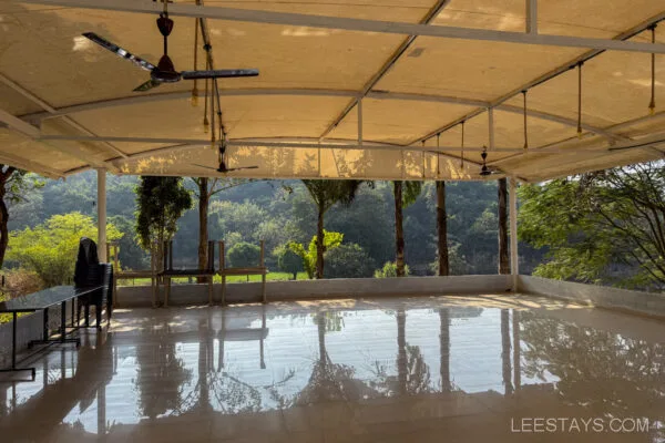 Spacious covered terrace at Lee Stay, Pawna, with shiny tiled floors, ceiling fans, and a scenic view of lush green trees and hills.