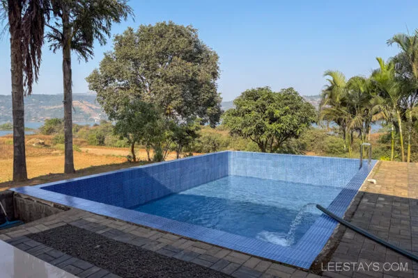 Scenic view of a small tiled swimming pool surrounded by palm trees, overlooking a serene landscape in Stay, Pawna, with hills and trees in the background.