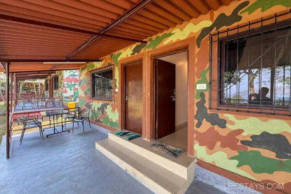 Outdoor seating area of a camouflaged-themed accommodation at Stay, Pawna, featuring a patio with tables and chairs under a corrugated metal roof.