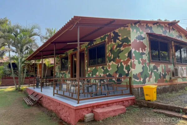 A camo-painted bungalow with a porch and outdoor seating, surrounded by palm trees, at Stay, Pawna.