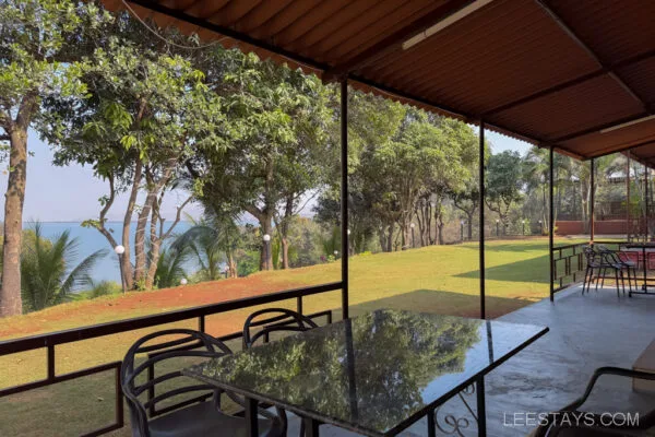 A serene outdoor seating area at Stay, Pawna, overlooking a lush garden with trees and a distant view of the lake under a clear blue sky.