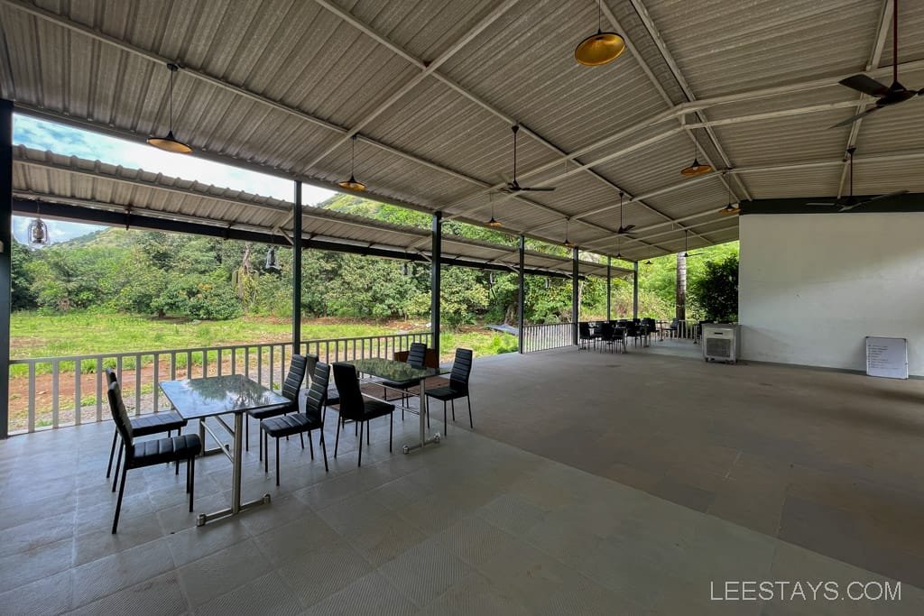 Spacious dining area of a resort in Lonavala featuring black chairs and glass tables, surrounded by lush greenery and open space.