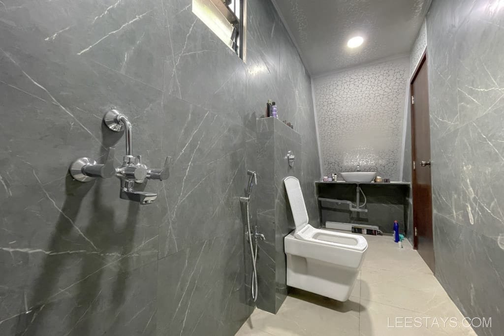 Modern bathroom in a Lonavala resort featuring gray marble walls, a sleek toilet, stylish sink, and contemporary fixtures for a luxurious experience.