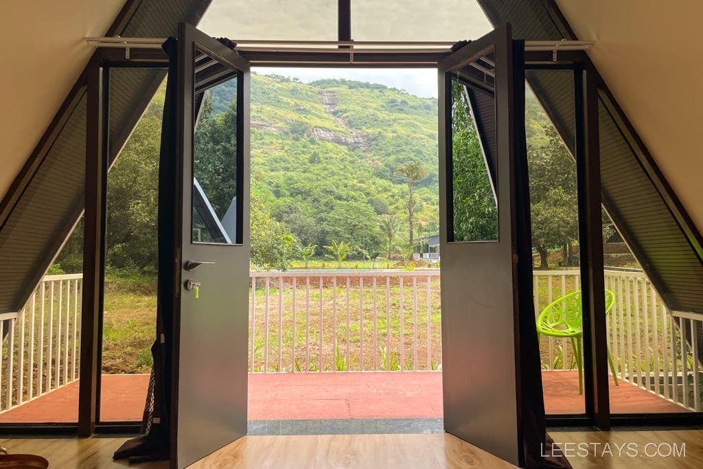 View from a resort in Lonavala, showcasing open doors leading to a green landscape with hills in the background and a vibrant chair on the porch.