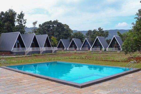 Modern resort in Lonavala featuring A-frame cabins set around a swimming pool, surrounded by lush greenery and scenic hills in the background.