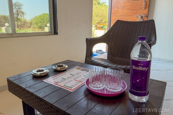 Interior view of a cottage in Lonavala featuring a wooden table with glasses and a bottle of water, overlooking a serene outdoor area.