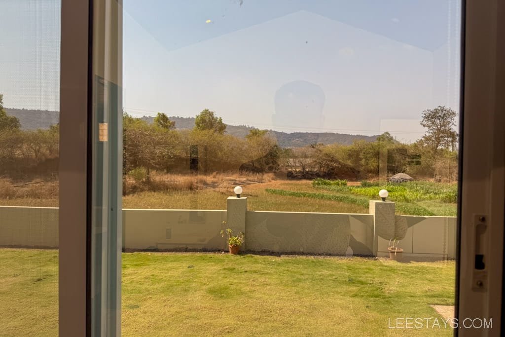 View of the grassy yard through a window with distant scenic hills and trees, typical of cottages in Lonavala, creating a serene atmosphere.