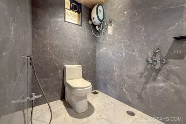 Modern bathroom with marble walls and silver fixtures in cottages, Lonavala. Features a toilet, water heater, and shower area.