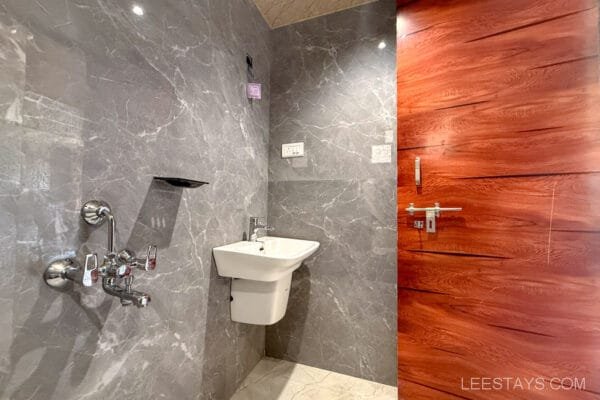 Modern bathroom in a Lonavala cottage featuring sleek gray marble walls, a white sink, and a wooden door, creating a luxurious and stylish look.